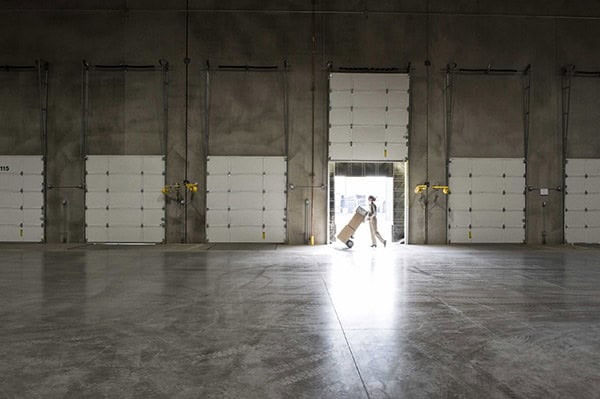 A warehouse worker with a hand truck at a loading dock door in a warehouse